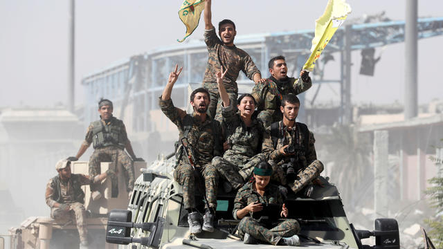 SDF fighters ride atop military vehicles as they celebrate victory in Raqqa 