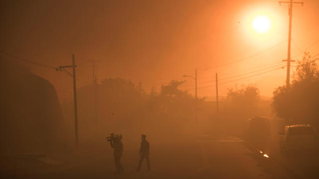 A TV crew walks through smoke as they work covering a  wind driven wildfire in Ventura, California 