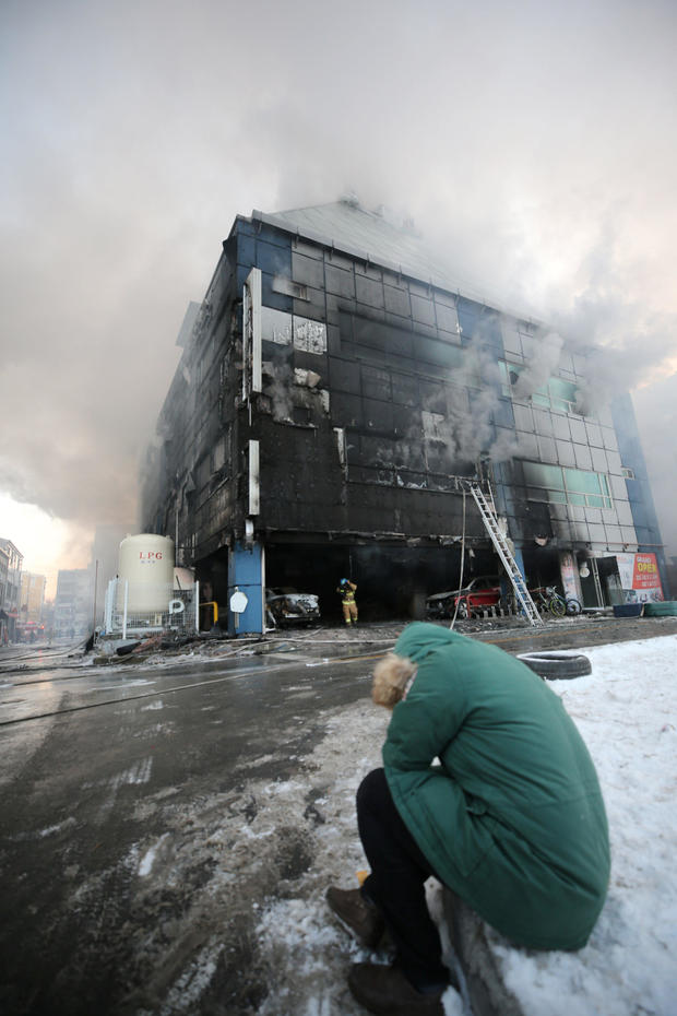 A man who is believed to be a relative of a victim reacts as smoke rises from a burning building in Jecheon 
