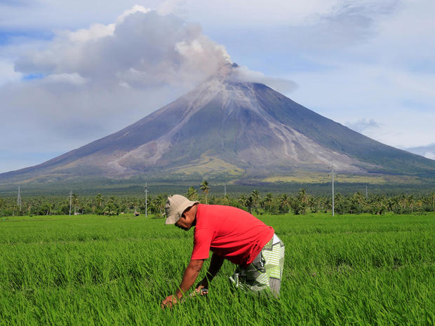 A farmer works on a rice farm while Mount Mayon volcano spews ash during a new eruption in Daraga 