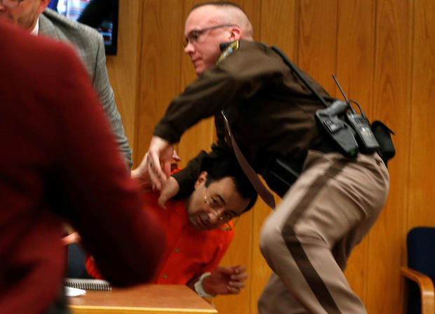 An Eaton County sheriff's deputy protects Larry Nassar, wearing orange, a former USA Gymnastics team doctor who pleaded guilty in November 2017 to sexual assault charges, as he is attacked by Randall Margraves, not pictured, during victim statements in hi 