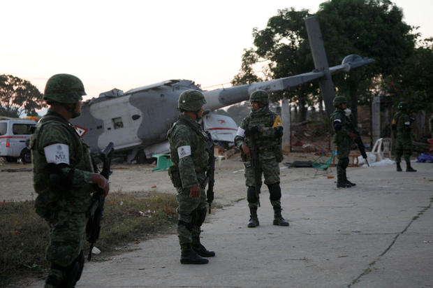 Soldiers stand guard next to a military helicopter, carrying Mexico's interior minister and the governor of the southern state of Oaxaca, crashed on top of two vans in an open field while trying to land in Santiago Jamiltepec 