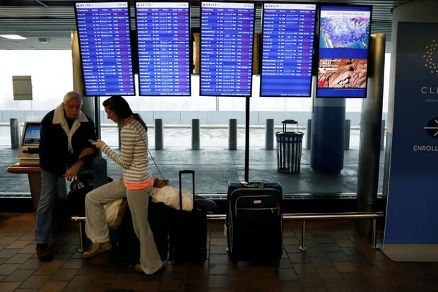 Air travelers sit with baggage next to Delta flight monitors showing canceled flights at LaGuardia Airport in New York March 21, 2018. 