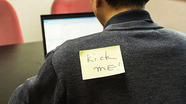 Office man with a yellow sticky note on his back, saying kick 