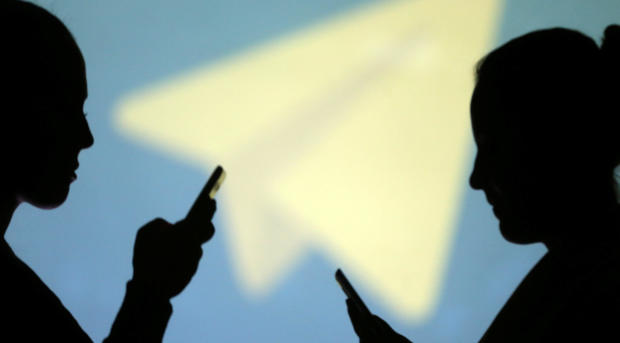 Silhouettes of mobile users are seen next to a screen projection of the Telegram logo in this picture illustration taken March 28, 2018. 