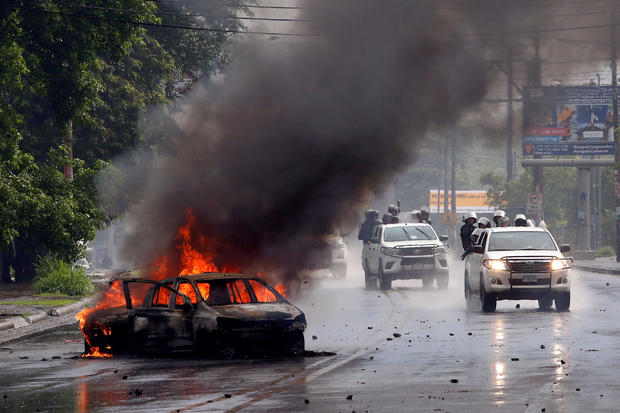 Riot police officers travel past a burning car during clashes with the anti-government protesters in Managua, Nicaragua 