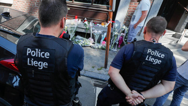 Belgian police officers pay tribute to the victims of a shooting outside of the cafe where the shooting took place in Liege 