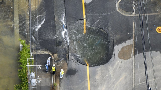 Water flows out from cracks in a road damaged by an earthquake in Takatsuki 