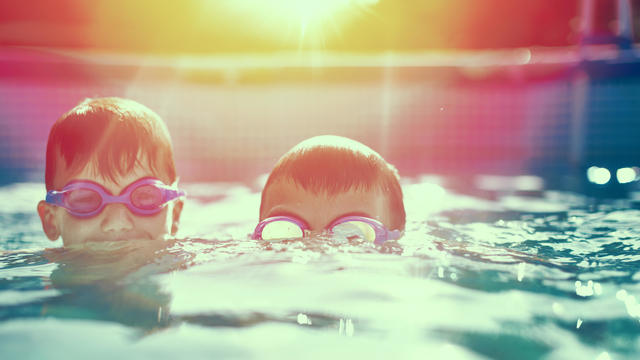 Two little kids in goggles swimming in pool at sunset 
