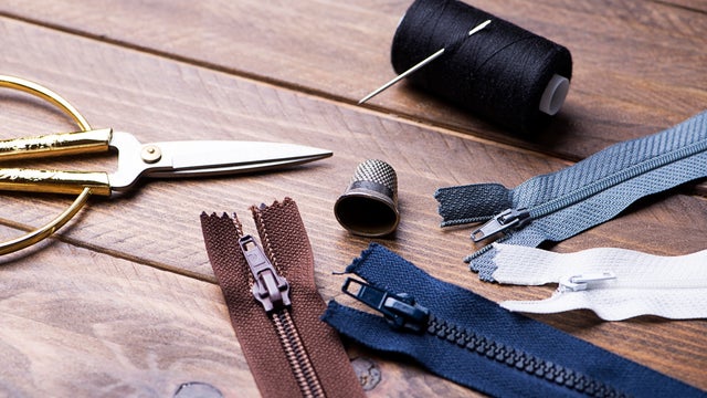 Scissors, tape measure, zipper, thread and needle next to thimble on wooden table. 