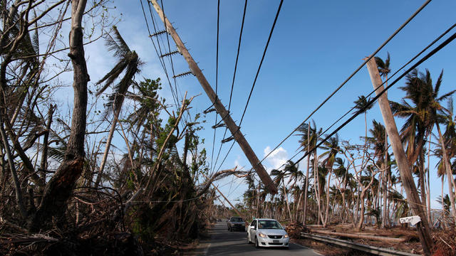 FILE PHOTO: Cars drive under a partially collapsed utility pole, after the island was hit by Hurricane Maria in September, in Naguabo 