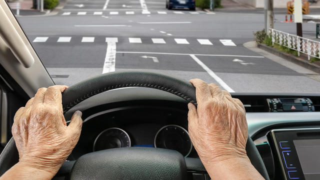 Senior woman driving a car on street in city. 