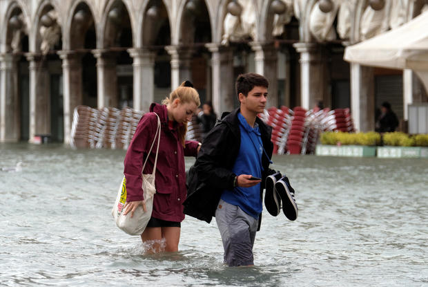 A couple walk on a catwalk in a flooded Saint Mark Square during a period of seasonal high water in Venice 