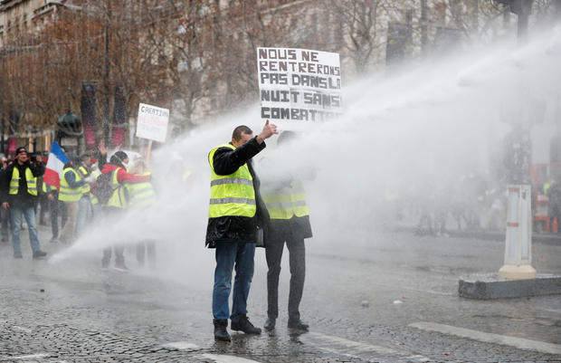 Protesters wearing yellow vest, a symbol of a French drivers' protest against higher fuel prices, stand up in front of a police water canon during clashes on the Champs-Elysees in Paris 