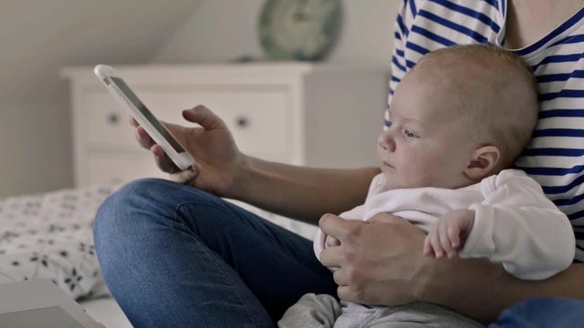 mother with baby, sitting on bed, smartphone 