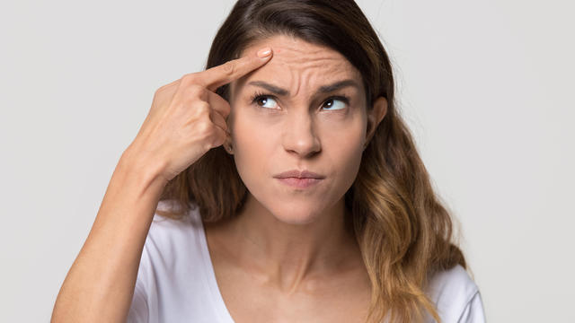 Depressed young woman touching forehead worried about skin wrinkle 