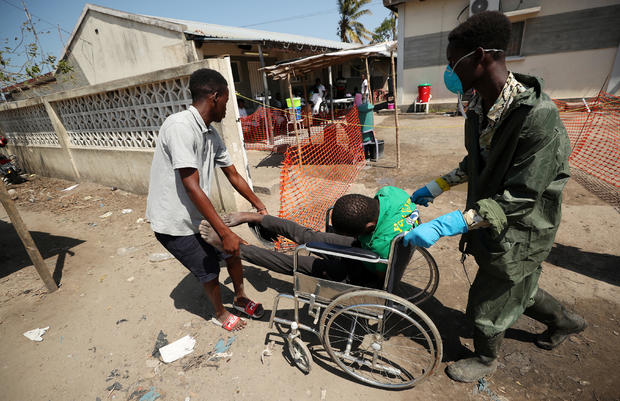 A medical staff member wears a protective mask as he assists a man arriving at a cholera treatment centre set up in the aftermath of Cyclone Idai in Beira 