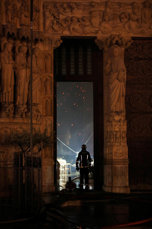 A Paris Fire brigade member is seen in a doorway as he looks into the Notre Dame Cathedral as a fire continues to burn in Paris 