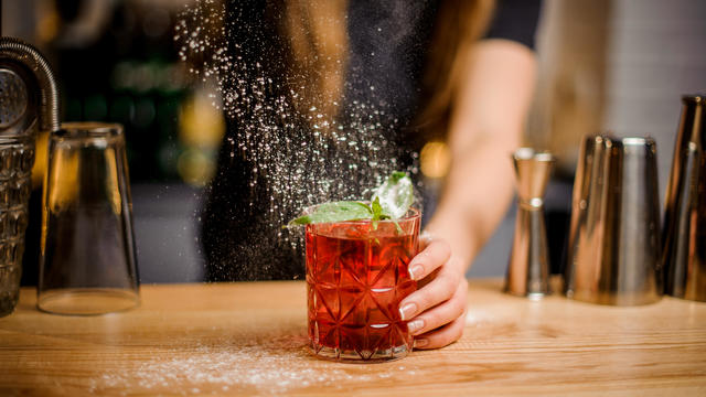 blondy barmaid finishes preparation of cocktail by adding a bitter of powdered sugar 