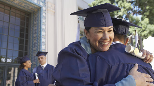 Female mature graduate student embracing colleague, outdoors, portrait 