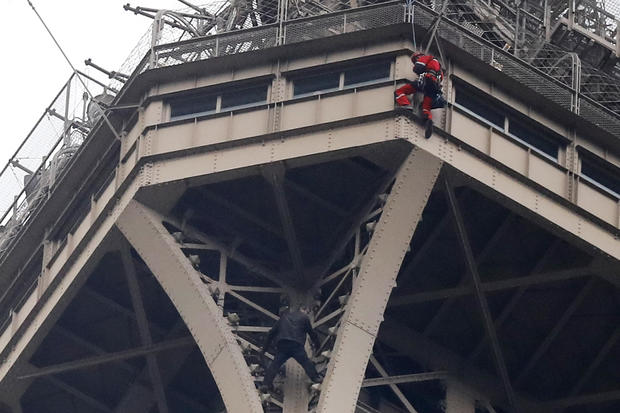 A rescue worker, top in red, hangs from the Eiffel Tower while a climber is seen below him between two iron columns May 20, 2019, in Paris. 