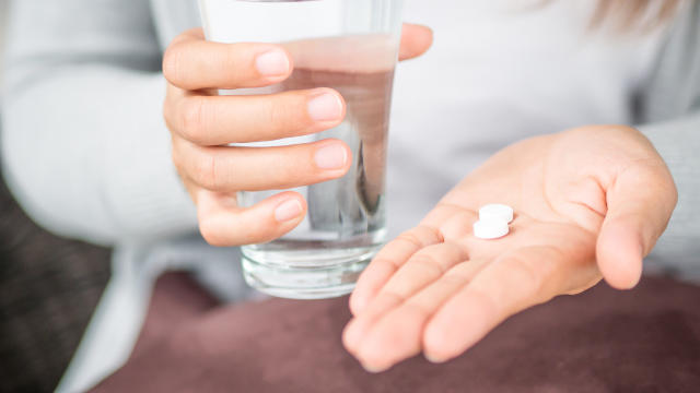 Closeup woman hand with pills medicine tablets and glass of water 