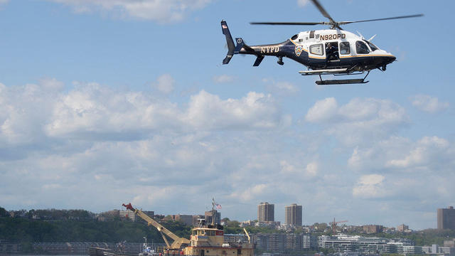 An NYPD helicopter flies over the site of a helicopter that crashed into the Hudson River is lifted on to the deck of an Army Corp of Engineers boat in New York 