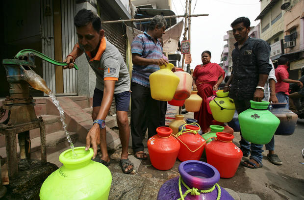 Man uses a hand-pump to fill up a container with drinking water as others wait in a queue on a street in Chennai 