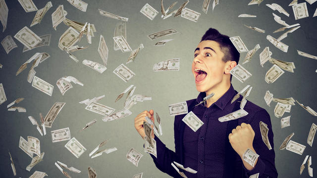 Man celebrates success under money rain falling down dollar banknotes 