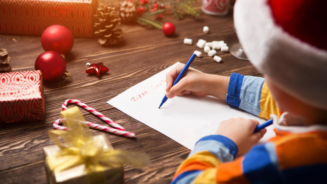 Child writes the letter to Santa Claus on wooden background with decorations. 