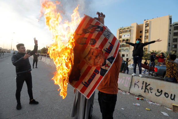 A protester holds a placard with an illustration of President Trump burning outside the U.S. Embassy in Baghdad, Iraq, January 1, 2020, during a protest to condemn airstrikes against an Iran-backed militia. 