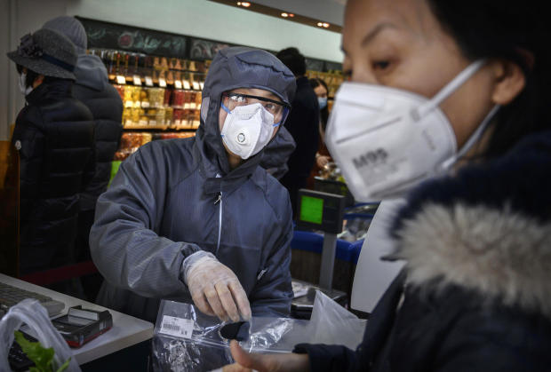A Chinese worker wears a protective suit and mask as she scans groceries for a customer at a supermarket on February 11, 2020, in Beijing, China. 