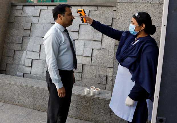 A private security guard uses an infrared thermometer to measure the temperature of a man at the entrance of a bank, following an outbreak of the coronavirus disease, in New Delhi 