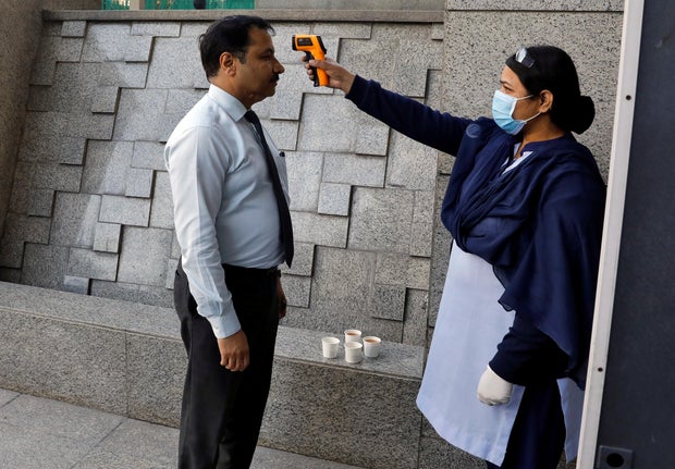 A private security guard uses an infrared thermometer to measure the temperature of a man at the entrance of a bank, following an outbreak of the coronavirus disease, in New Delhi