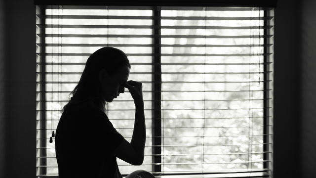 Tired woman standing next to bedroom window. 