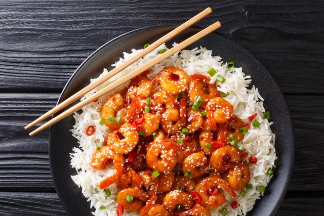 Fried sticky shrimps with garlic, chilli, sesame seeds and green onions served with rice close-up in a plate. Horizontal top view 