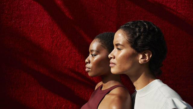 Side view of women standing against red wall 