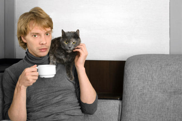 young man in a gray sweater with a Cup of coffee in his hands and his gray cat 