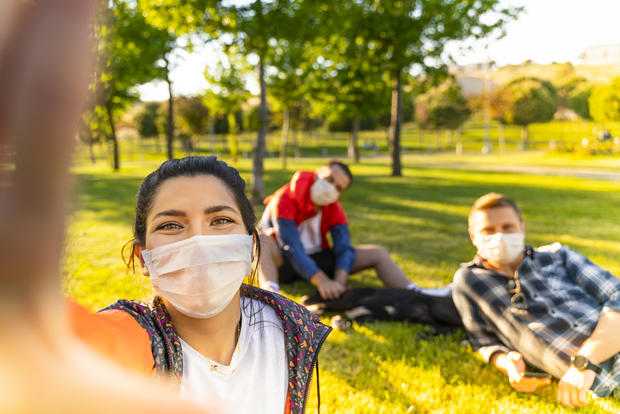 face mask Cheerful university student taking selfie with friends sitting on grass 