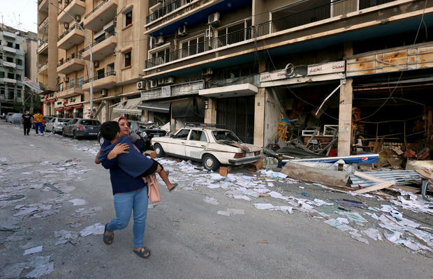 A woman carries a child as she walks past damaged shops following Tuesday's blast in Beirut 