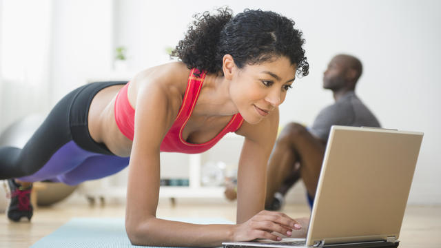 Woman using computer and doing push-ups in gym 