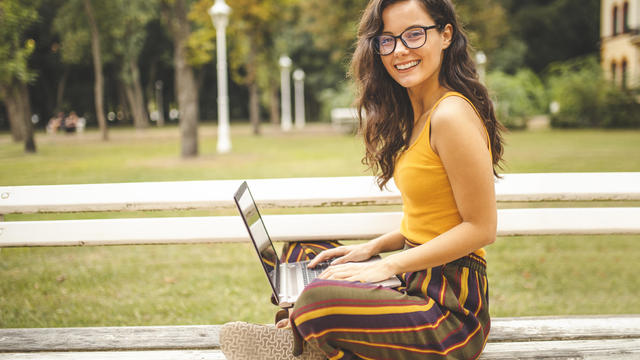 Woman using laptop and sitting on park bench 