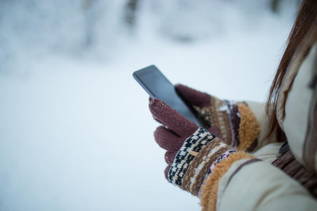 Female hands holding a cellphone outdoors in the snow 