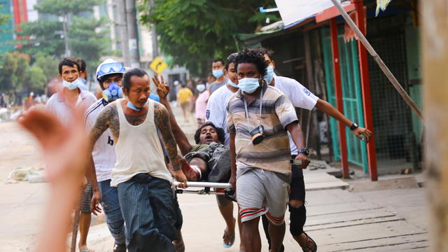 A man who was shot during the security force crackdown on anti-coup protesters shows a three-finger salute as he is helped in Thingangyun, Yangon 
