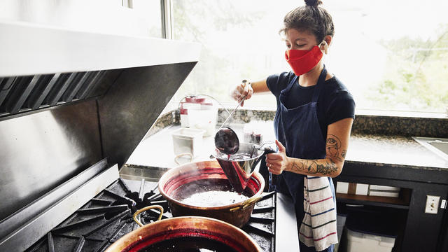 Female chef ladling freshly made organic jam into sieve before putting in jars 