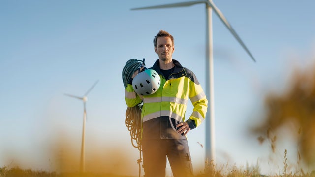 Technician standing in a field at a wind farm with climbing equipment 