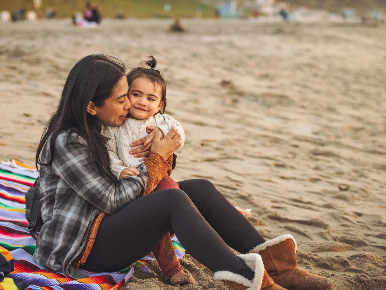 Mother Holding Baby Girl On Beach Sand 