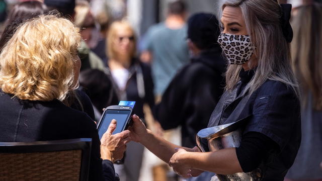 A masked worker deals with a customer at an outdoor sidewalk restaurant in Encinitas 