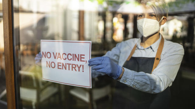 Restaurant owner holding a sign showing that they wish customers, who are vaccinated against COVID-19 to come in the restaurant. 