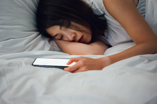 Young woman asleep next to smart phone on bed 